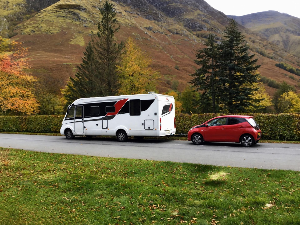 Motorhome towing a red car with TowGlide in a mountain setting